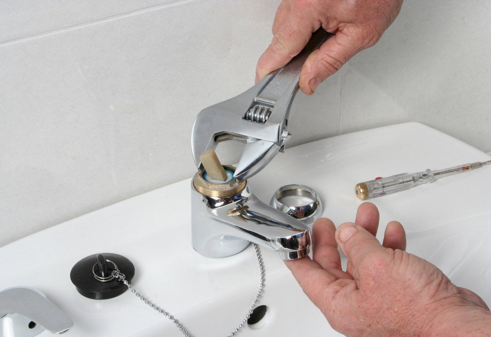 A person is fixing a faucet with a wrench.