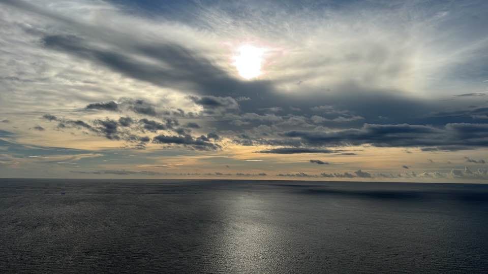 Sun breaking through clouds over calm ocean.