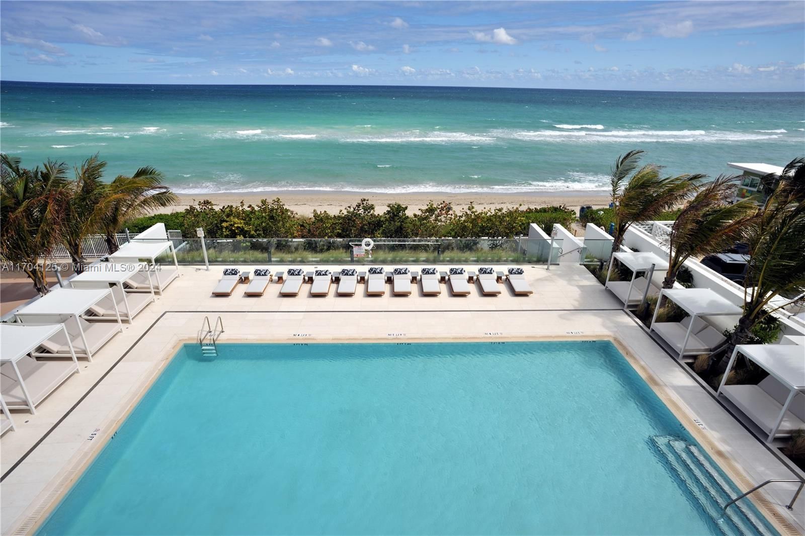 Pool overlooking ocean; white cabanas, turquoise water, sunny day.