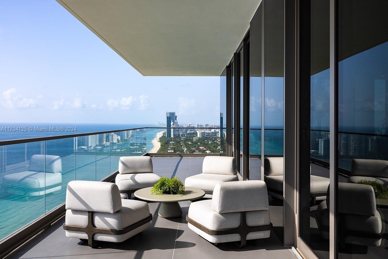 Balcony with modern outdoor furniture overlooking ocean and city. Blue sky and water.