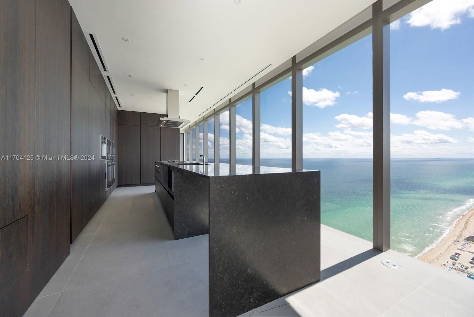 Modern kitchen with ocean view; dark cabinetry, island, and large windows.