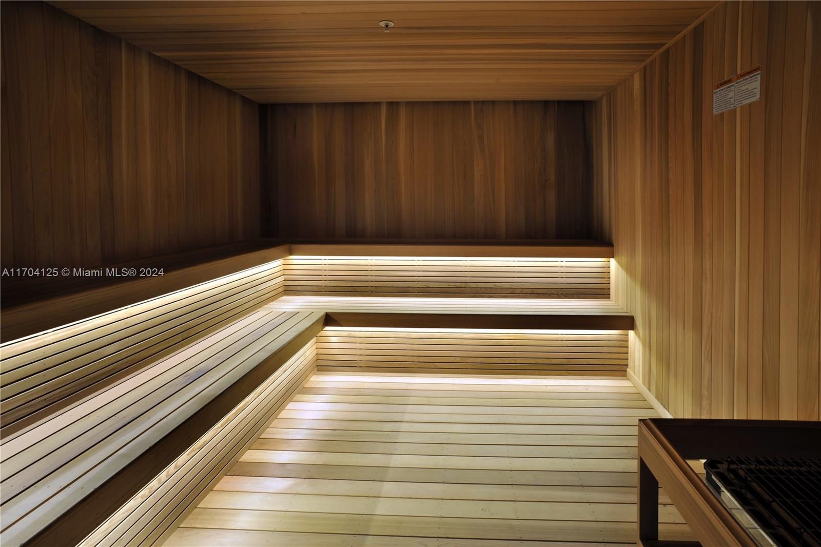 Wooden sauna with three-tiered benches, soft lighting, and a small wooden bench in the foreground.