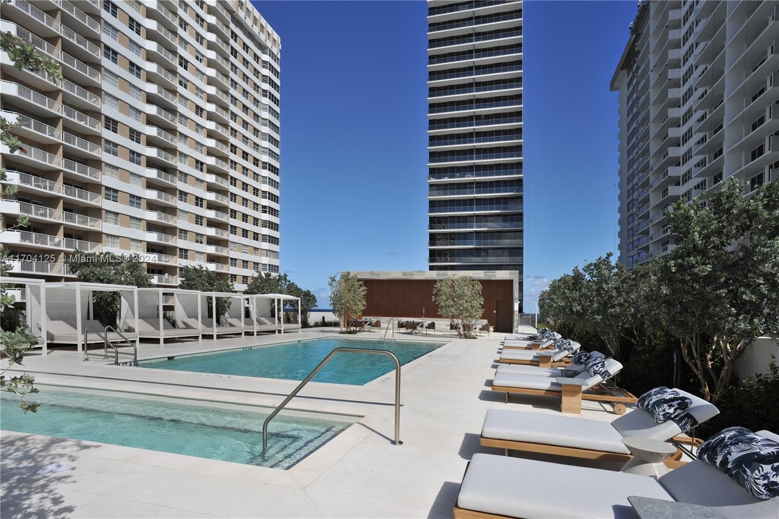 Swimming pool and lounge chairs between two high-rise buildings, blue sky overhead.