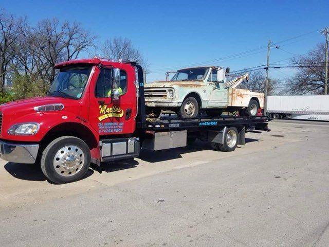 Red tow truck carrying a weathered white pickup truck on a bright day. Red tow truck carrying a weathered white pickup truck on a bright day.
