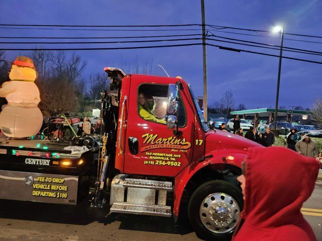 Red tow truck with a snowman on the back, in a nighttime parade.