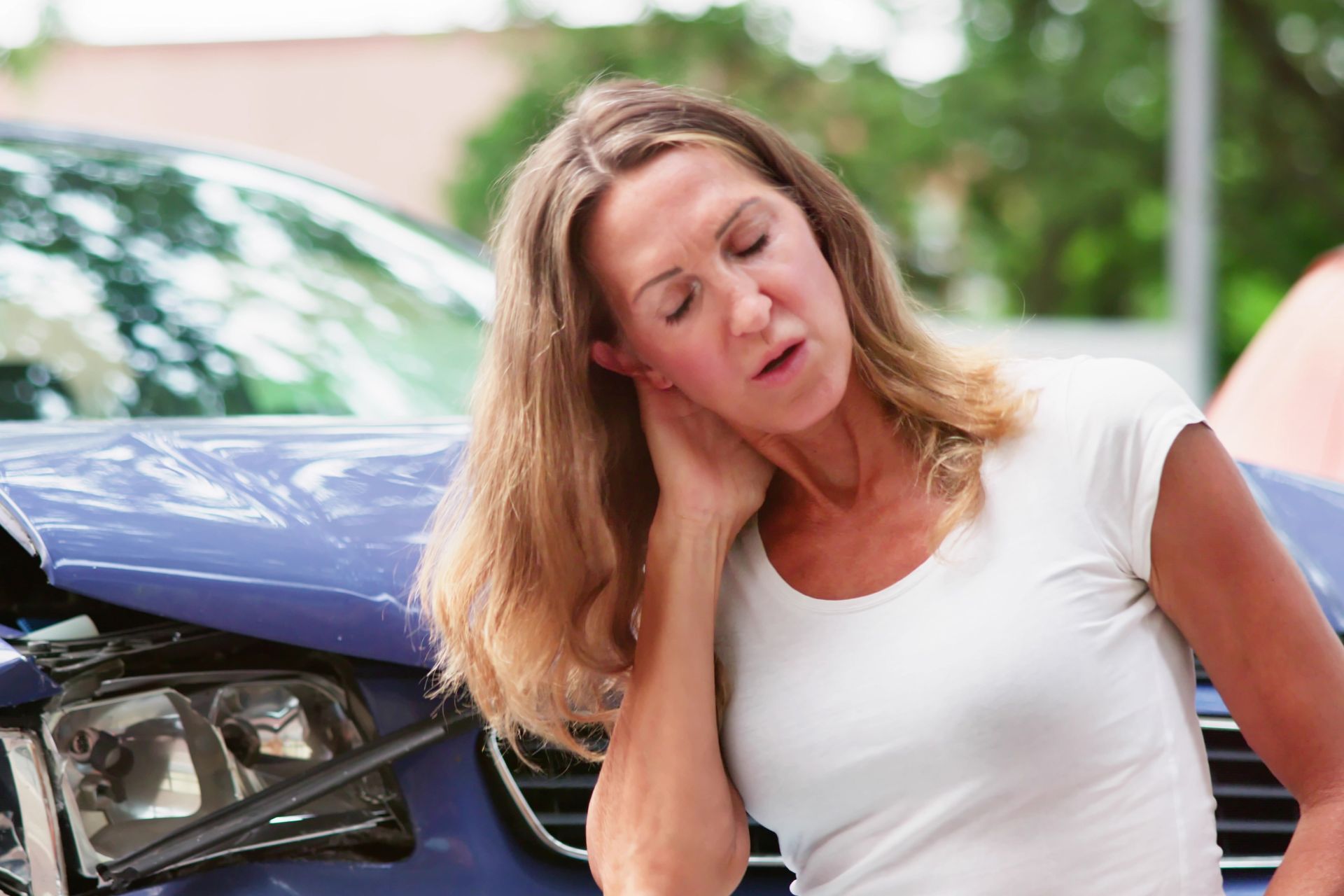A woman is sitting in front of a damaged car.