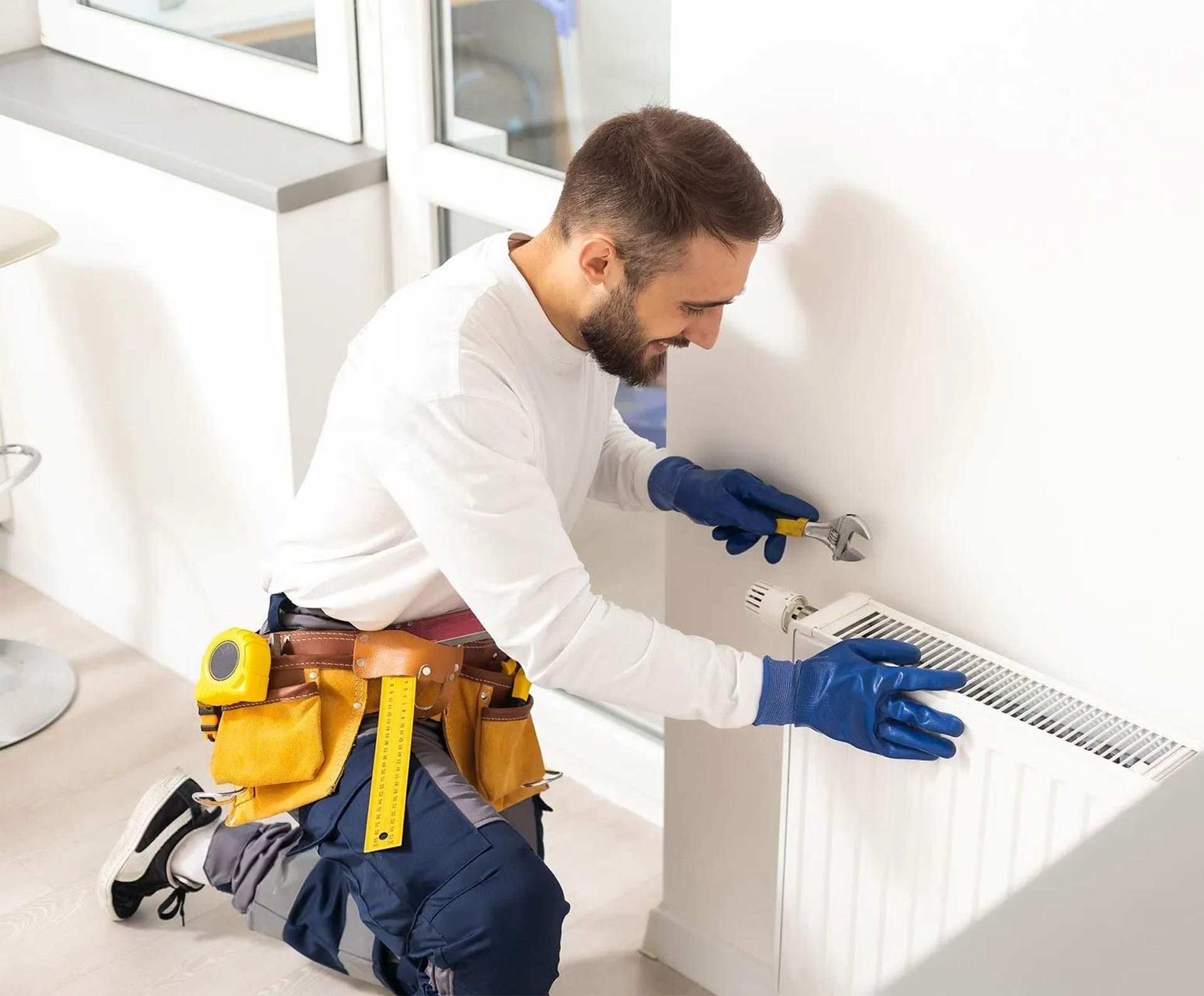 A man is kneeling down fixing a radiator in a room.