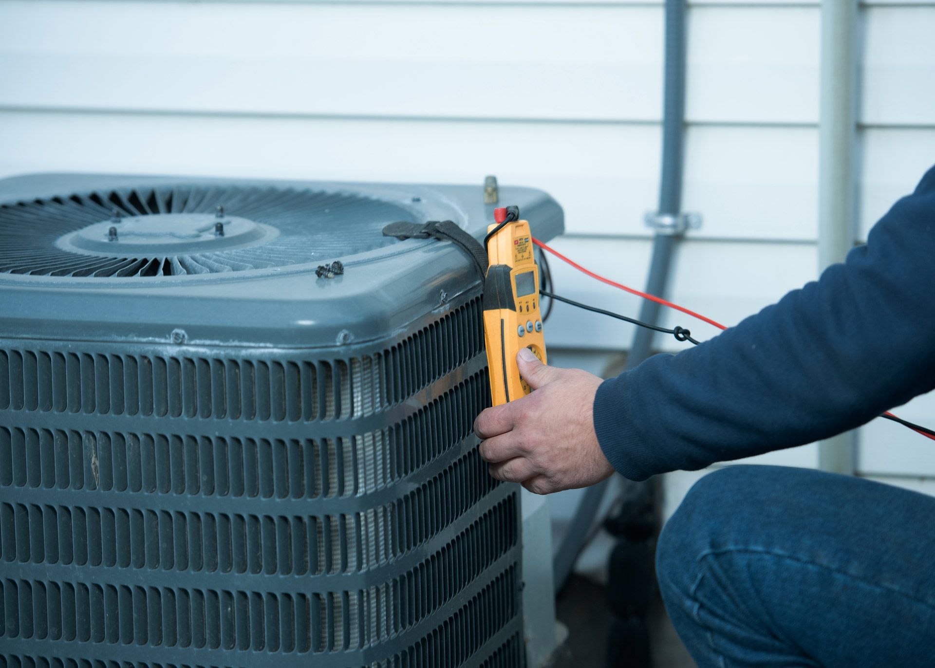 A man is working on an air conditioner outside of a house.