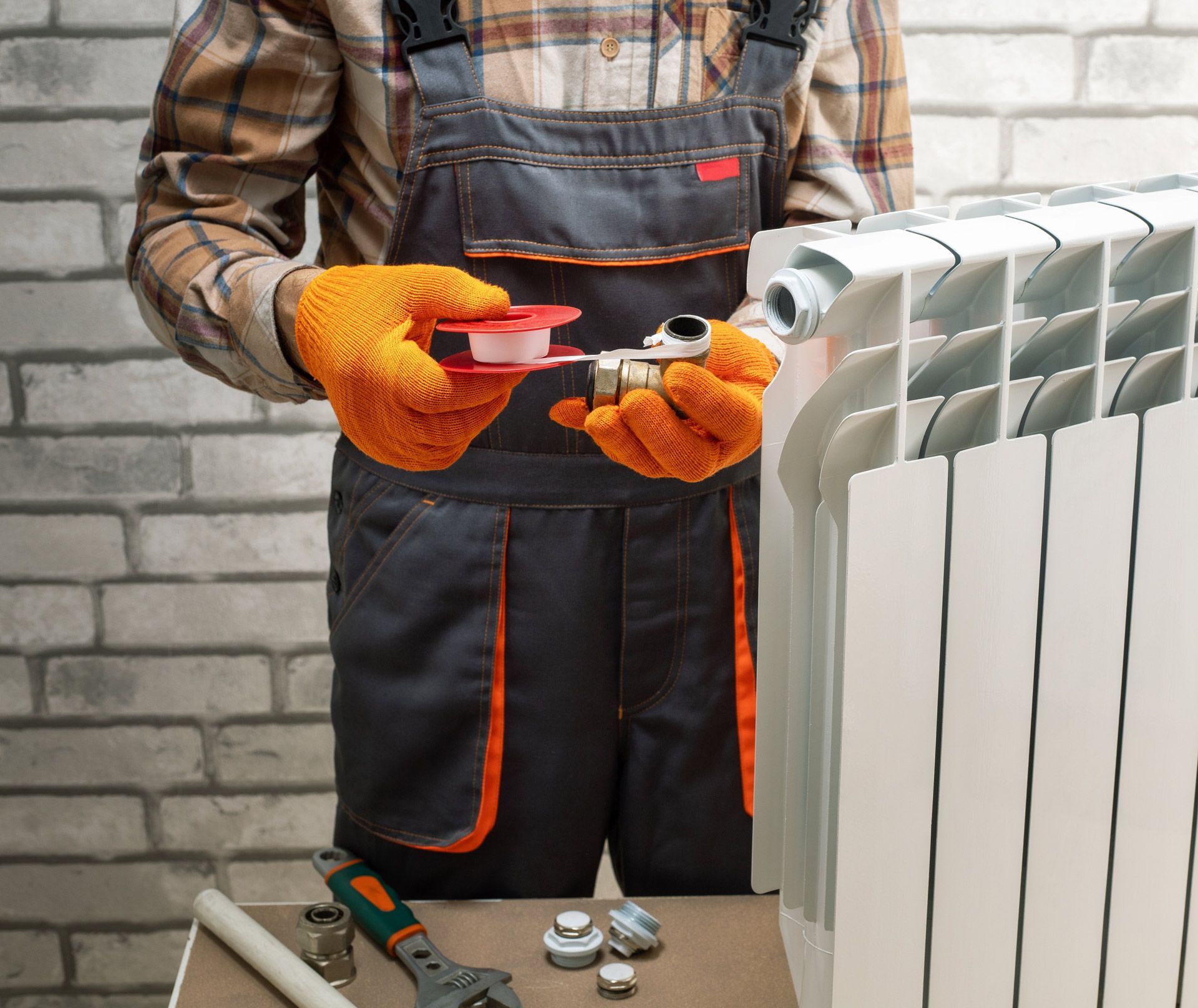 A man is fixing a radiator with a wrench and tape.