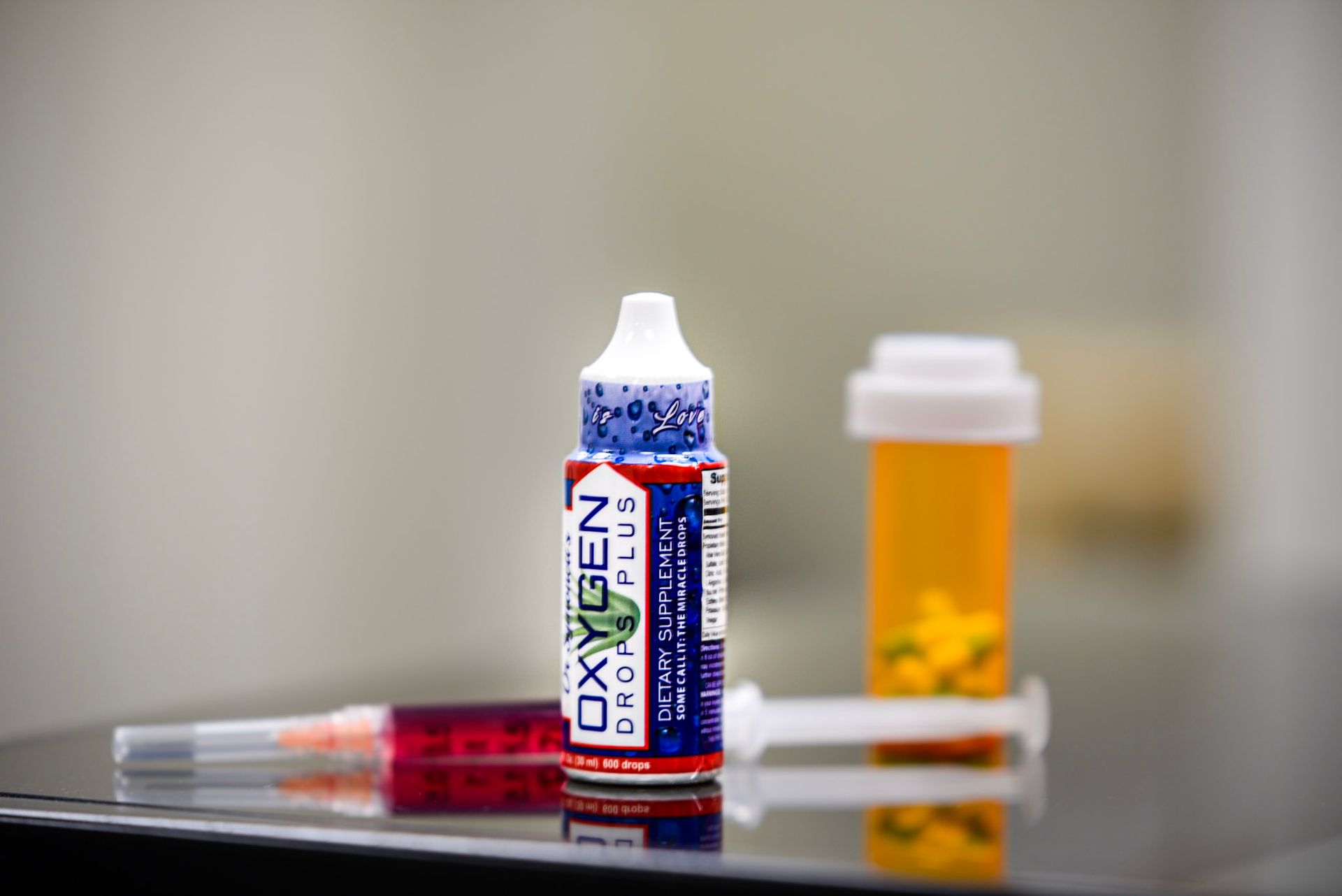 A bottle of oxygen next to a syringe and a bottle of pills on a table.