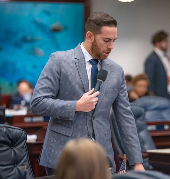 A man in a suit and tie is speaking into a microphone