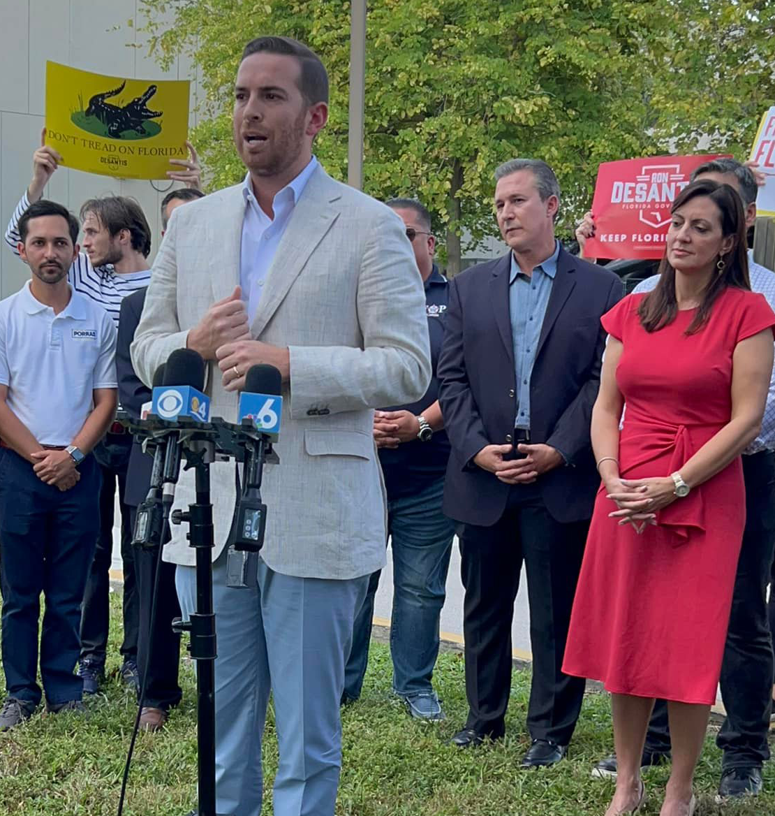 A man in a suit stands at a podium in front of a crowd