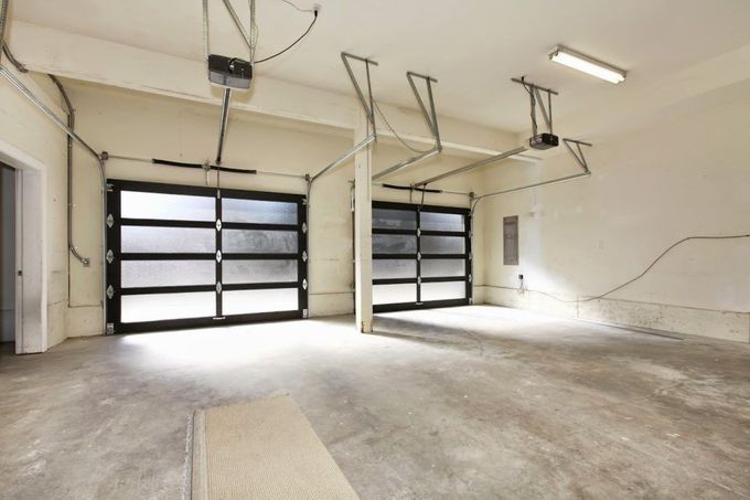 Empty garage with two dark glass doors, concrete floor, and overhead openers.