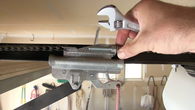 Hand using a wrench to tighten a part of a garage door opener in a garage.