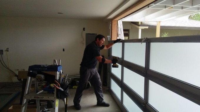 A man installing a frosted glass garage door using a power drill inside a garage.