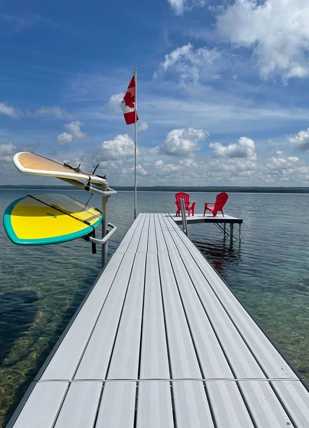 A long aluminum dock featuring a double kayak rack, flag pole and chairs overlooking clear waters