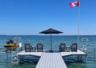 An image of a aluminum custom dock featuring various chairs, an umbrella, flag pole, a pwc lift and boat lift