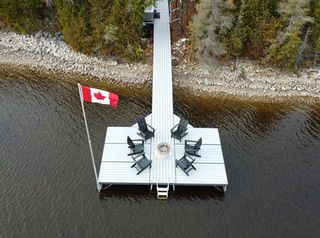 An aerial view of a very long aluminum custom dock with a firepit and chairs placed around it