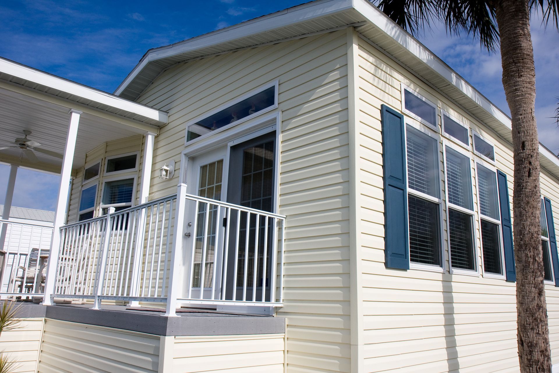 Beige house with blue shutters and a porch, under a blue sky.