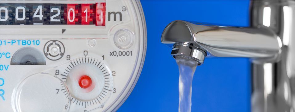 Plumber in blue plaid shirt records water meter reading on clipboard in a building.