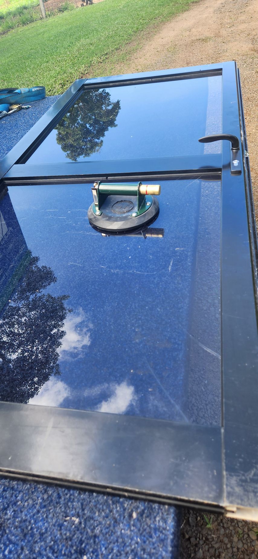 Dark blue glass panel with a handle and suction cup for lifting. Reflection of sky and trees 