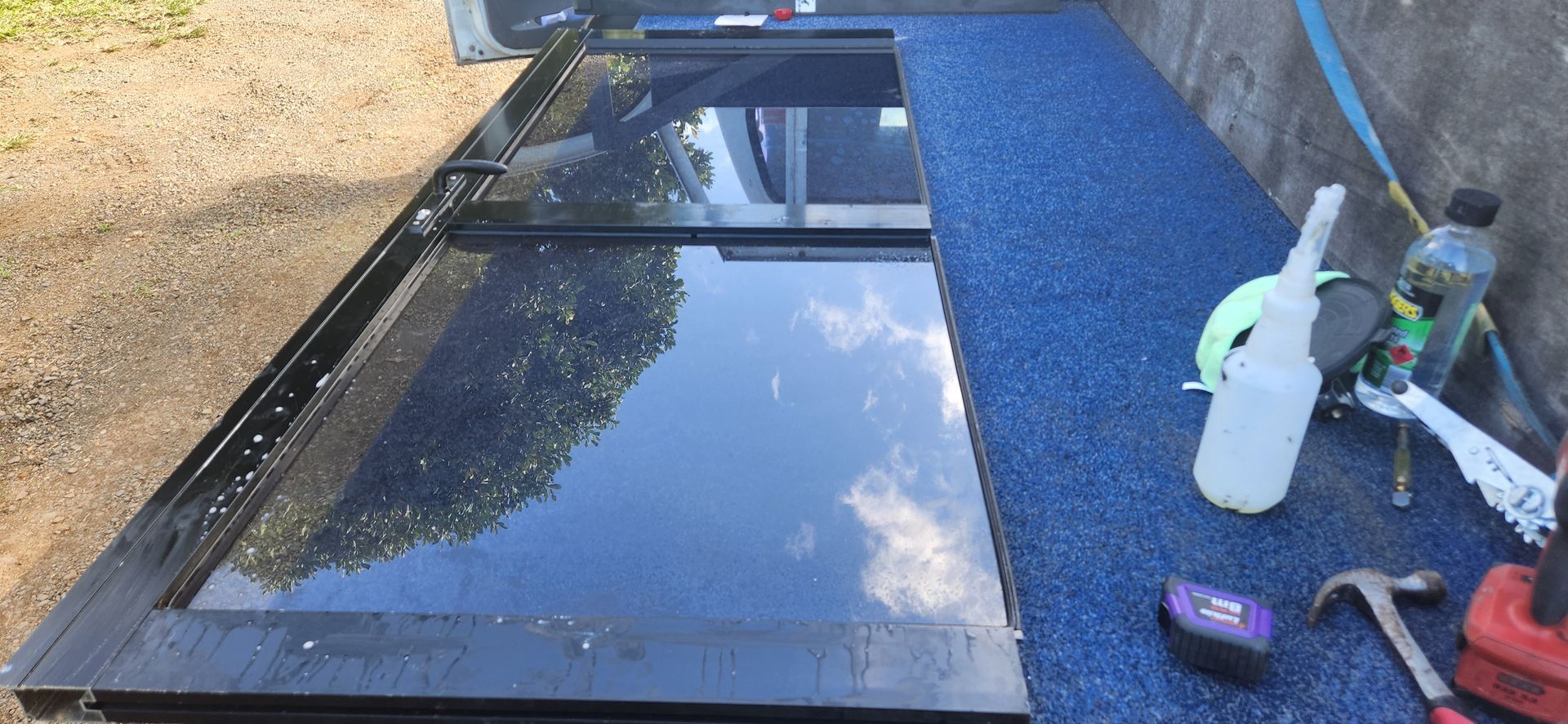 A black truck bed with a reflective surface and blue mat, tools, and bottles alongside - Advancetech Glass & Glazing in Wulguru, QLD  