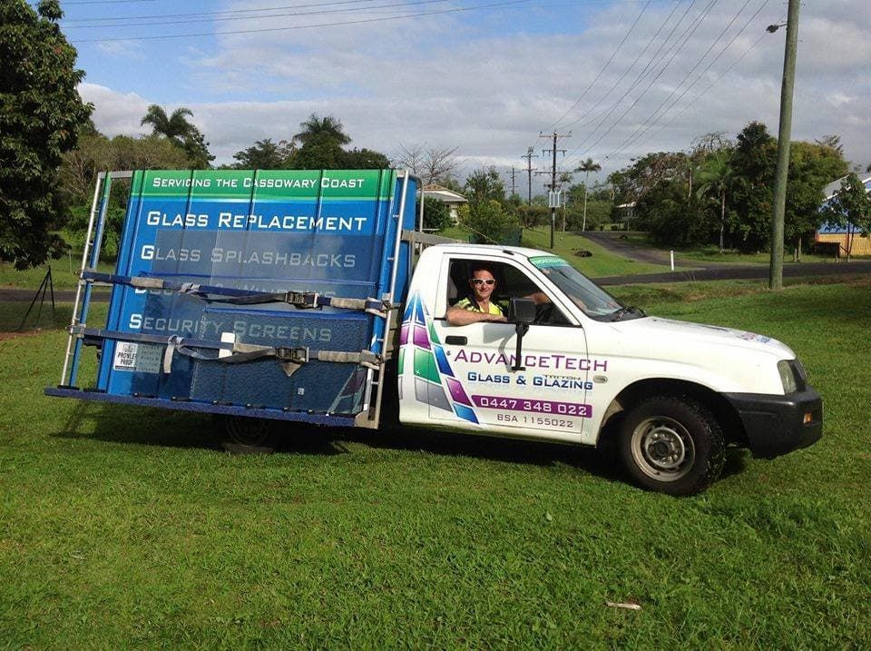 White truck with glass rack, parked on grass. A person smiles from the driver’s seat. 