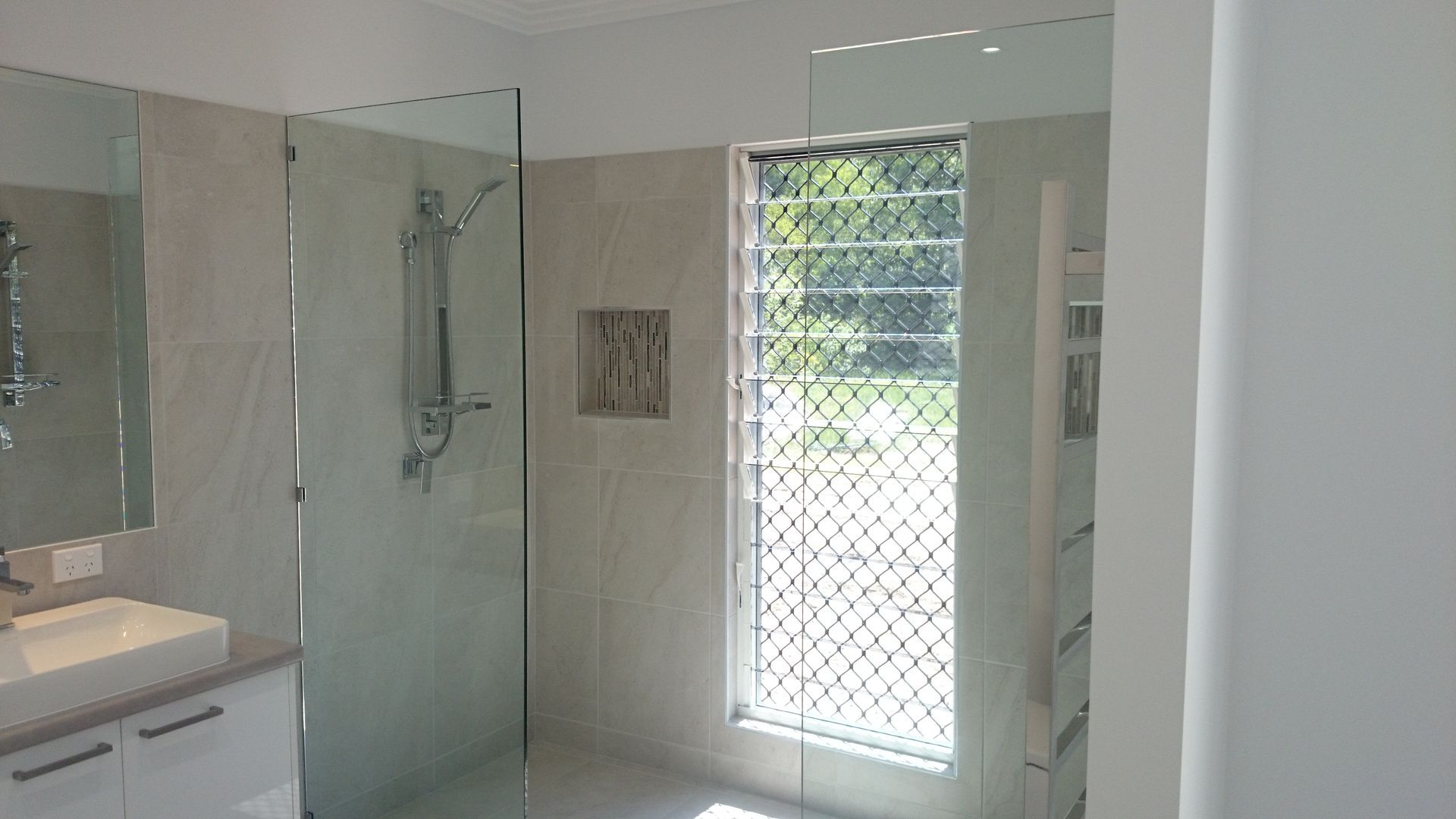 Modern bathroom with glass shower, vanity, and a window with security bars — Advancetech Glass & Glazing in Wulguru, QLD 