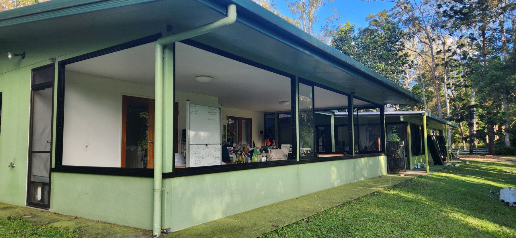 Green House With Large Windows, A Covered Patio, And Lush Green Lawn — Advancetech Glass & Glazing in Wulguru, QLD