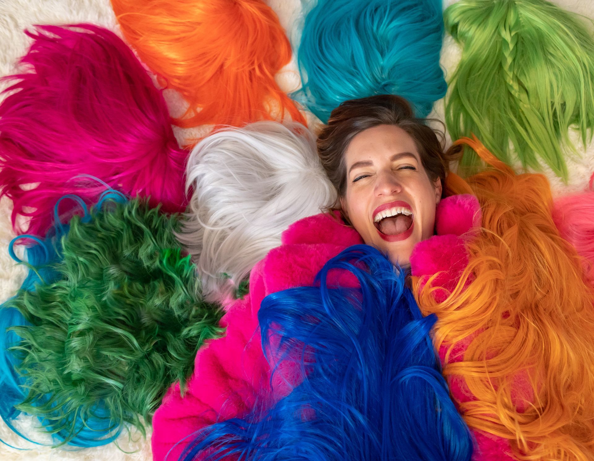 The face of the artist, laughing, in a pile of her wigs from 2023.