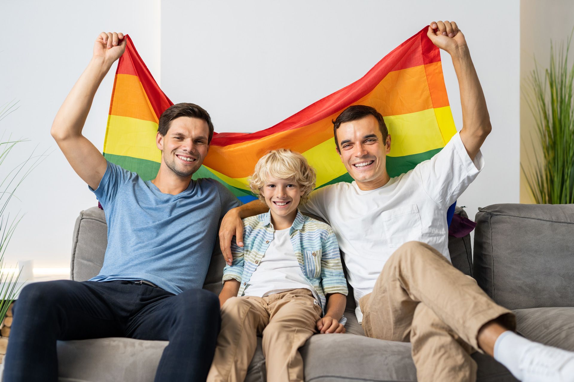 three men and a boy are sitting on a couch holding a rainbow flag .