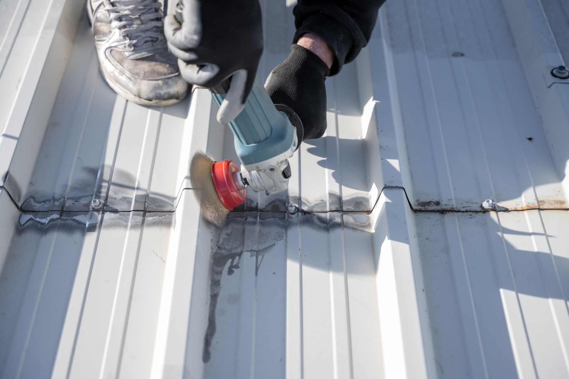 Worker using a power tool to grind and clean seams on a metal roof, preparing the surface. Worker using a power tool to grind and clean seams on a metal roof, preparing the surface.