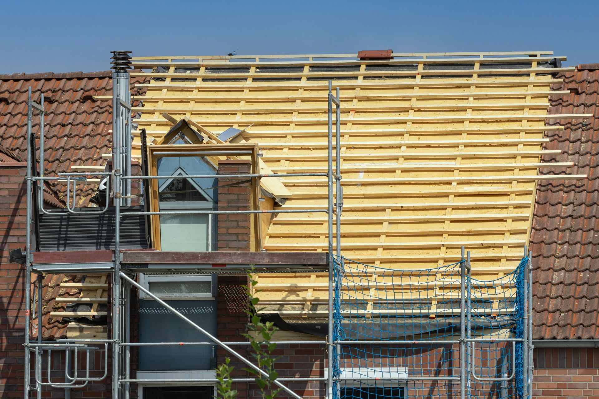 Active re-roofing project on a brick house with exposed wood battens and metal scaffolding. Active re-roofing project on a brick house with exposed wood battens and metal scaffolding.
