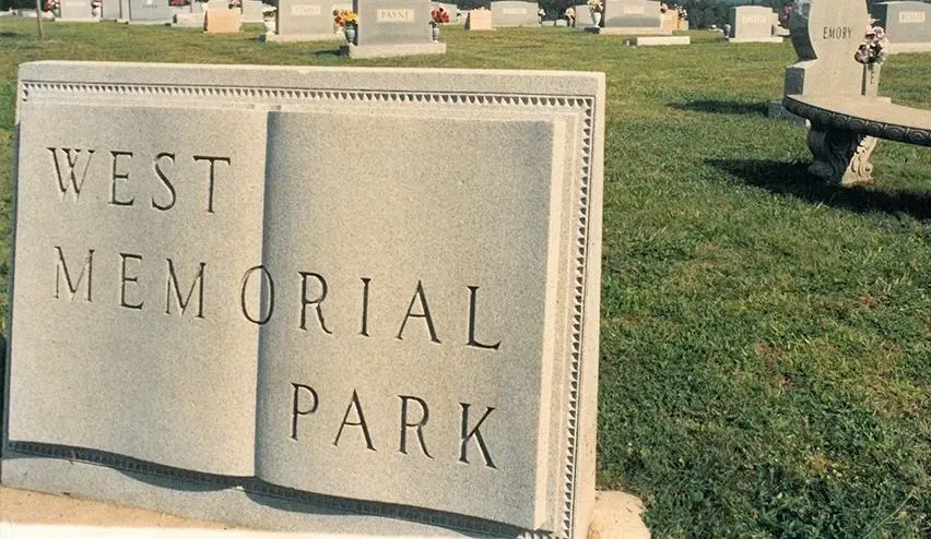Stone sign reading “West Memorial Park” on a grassy lawn.