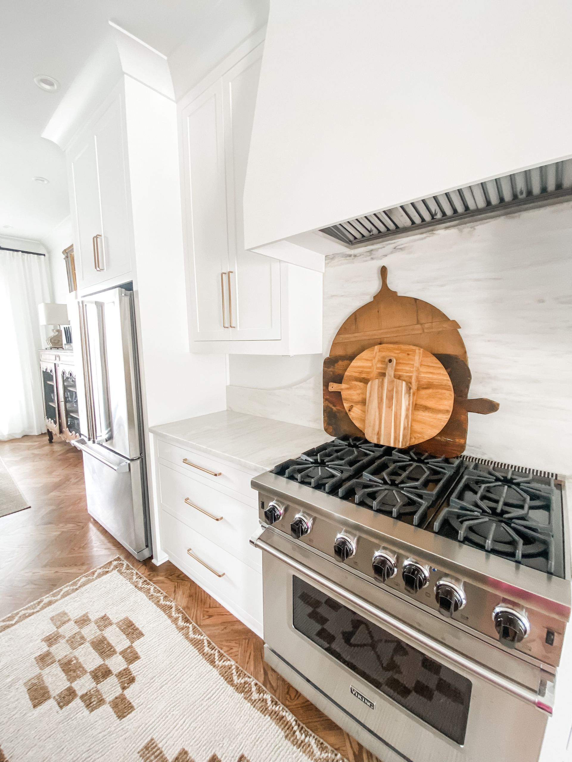 White kitchen with stainless steel oven, cutting boards, and decorative rug.