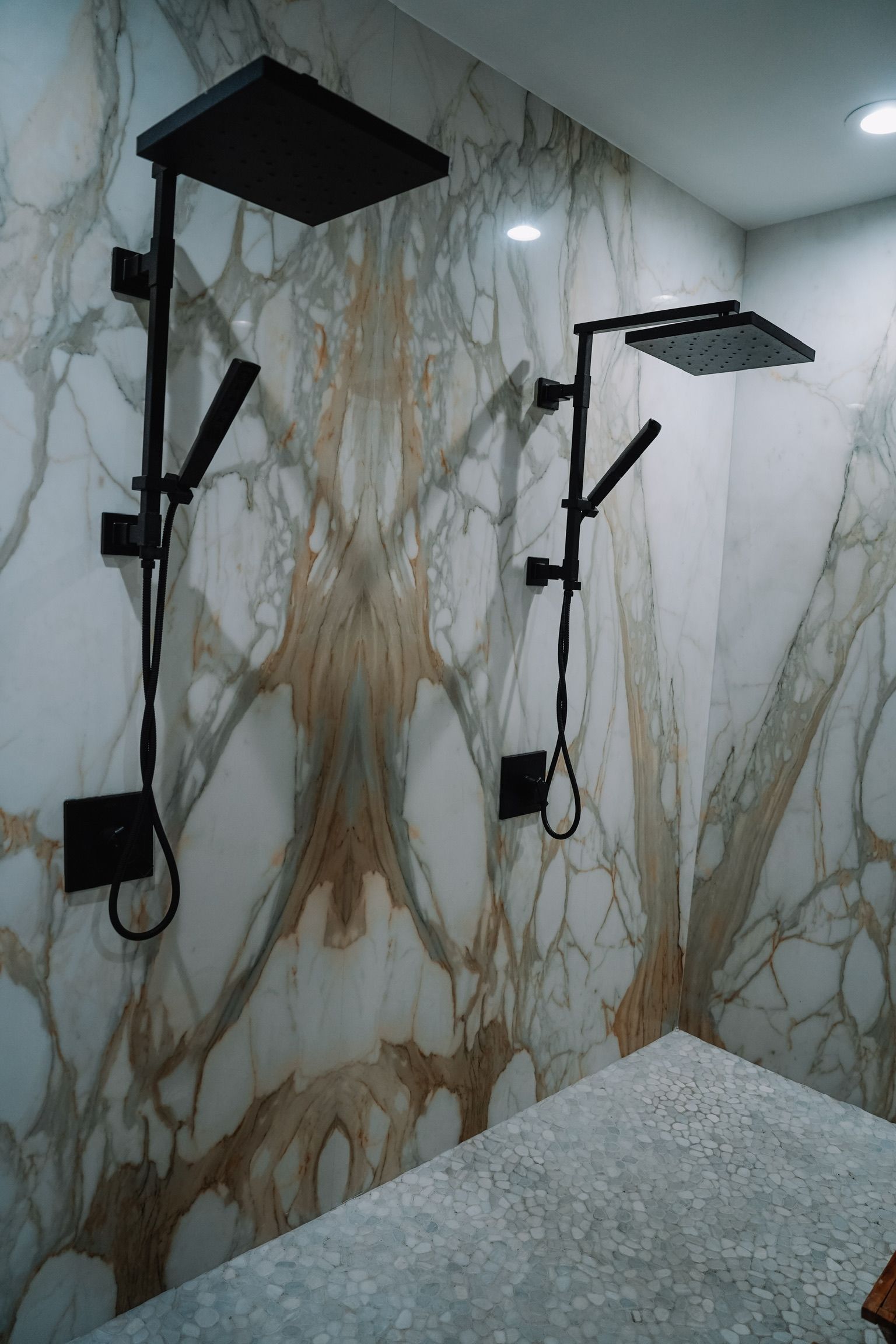 Two black showerheads with handheld wands on a marble-patterned wall.