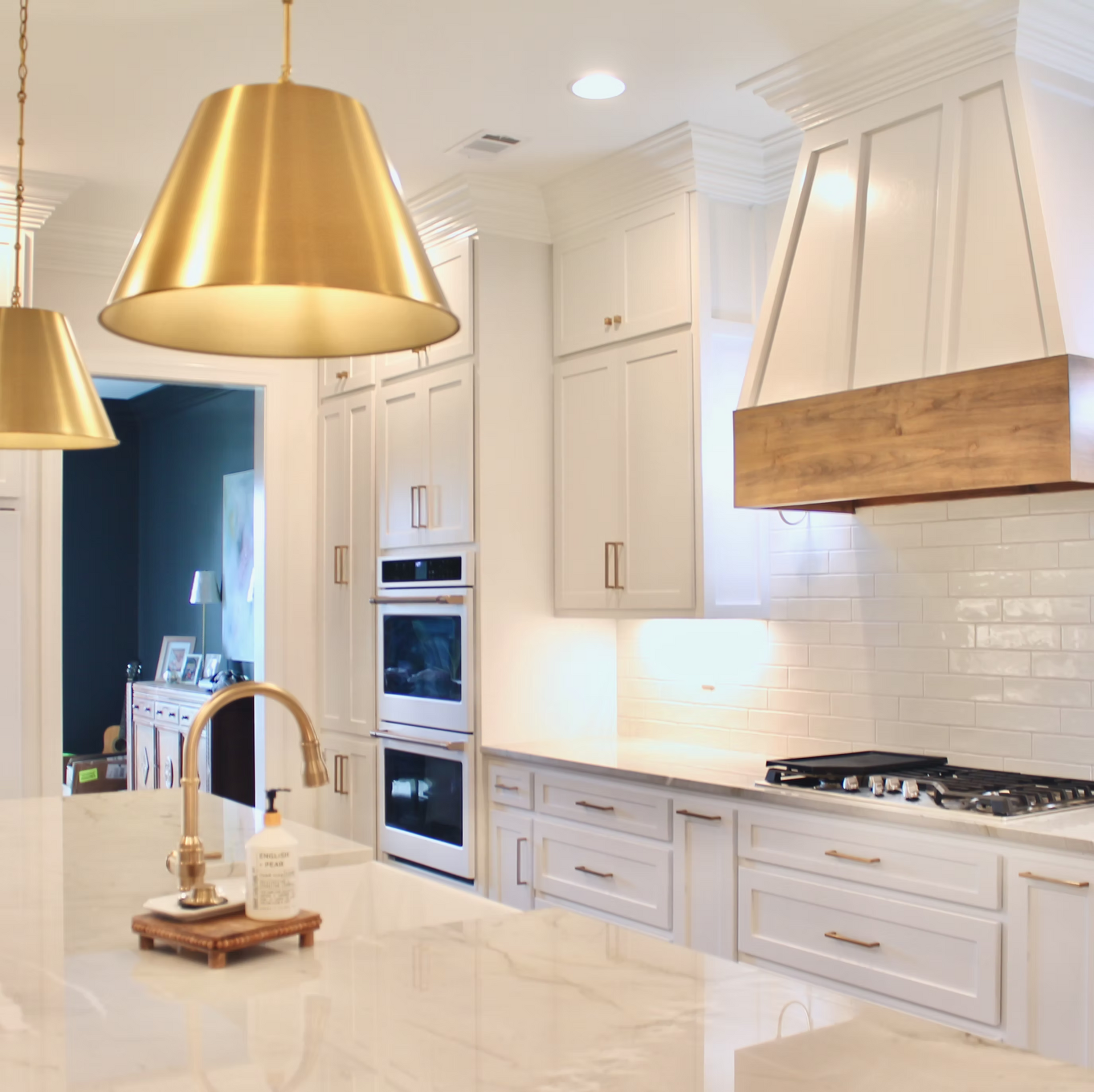 A bright white kitchen with gold accents. Includes a large island, stove, and range hood with wood trim.