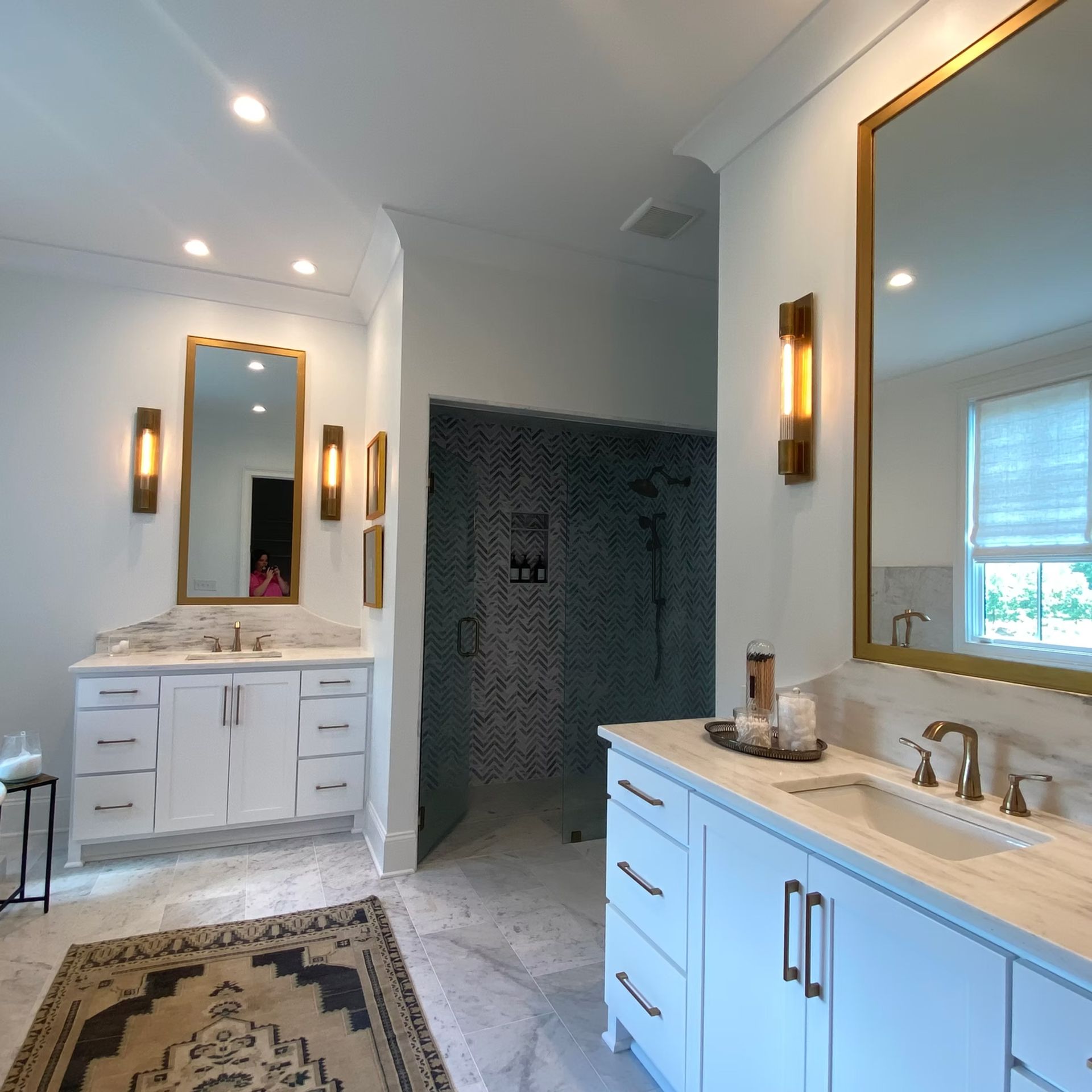 Elegant bathroom with white cabinets, gold mirrors, marble countertops, and a mosaic-tiled shower.