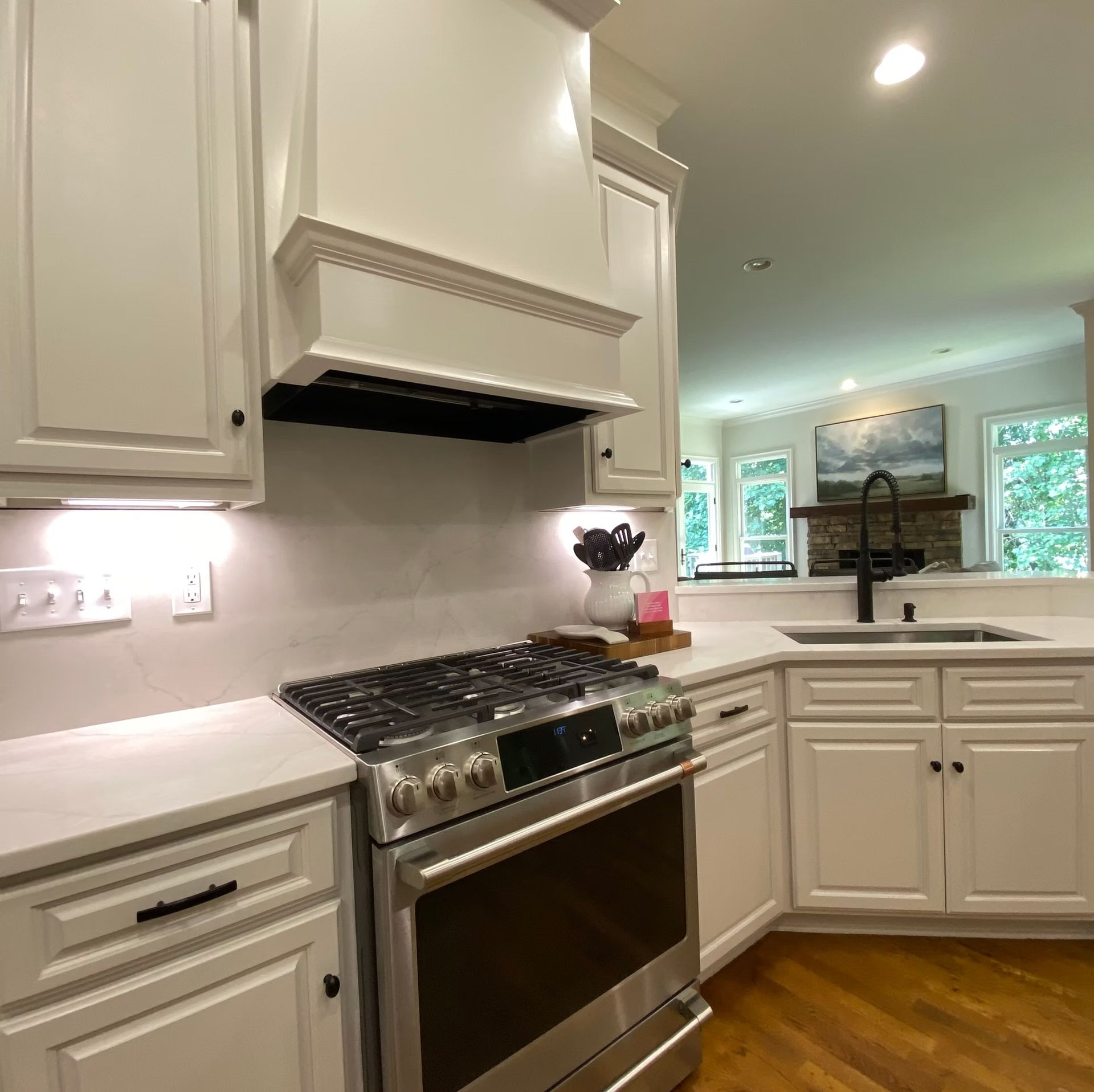 White kitchen with stainless steel oven, cabinets, and a view into a living room.