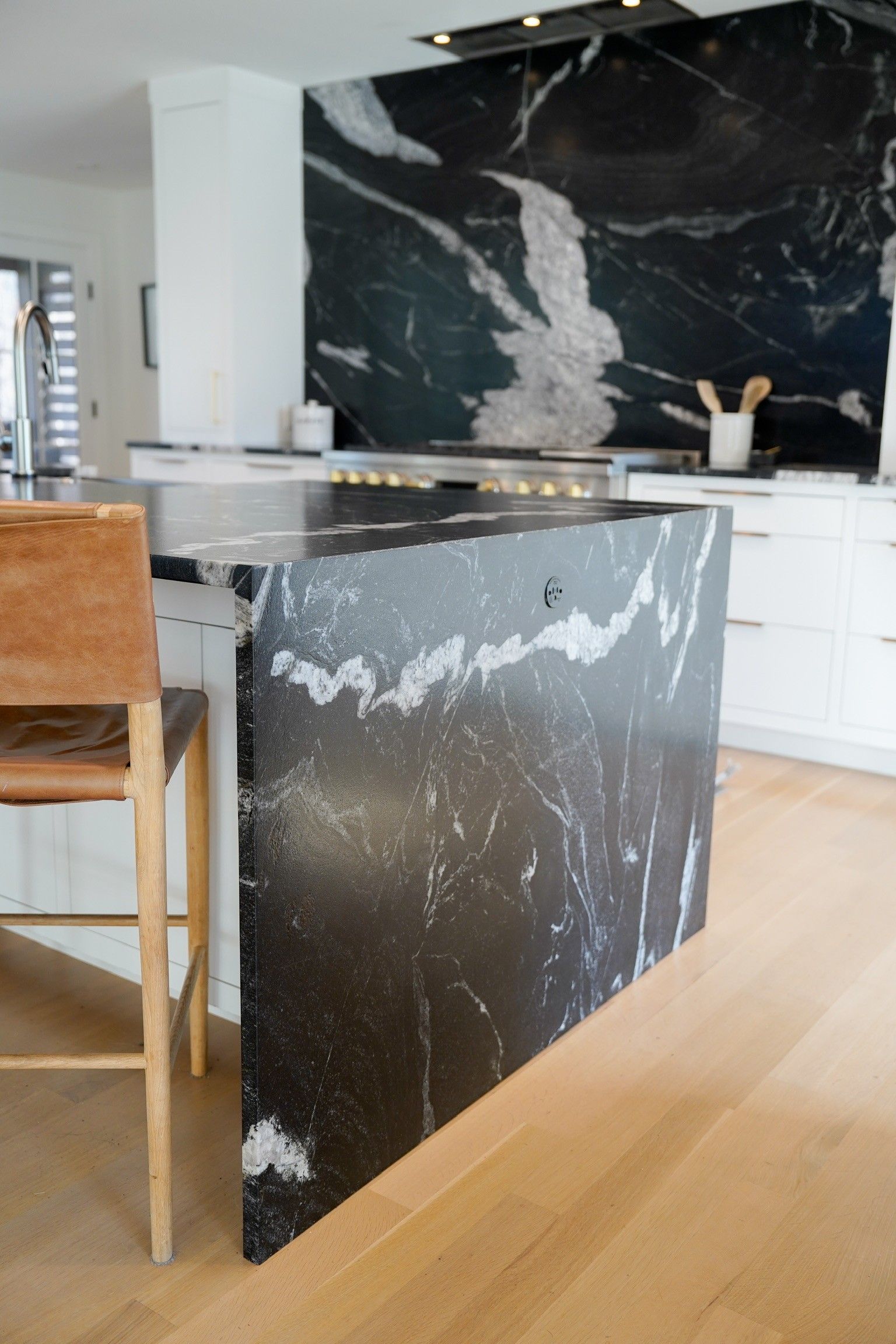Kitchen with a black marble island and backsplash, light wood floors, and white cabinets.