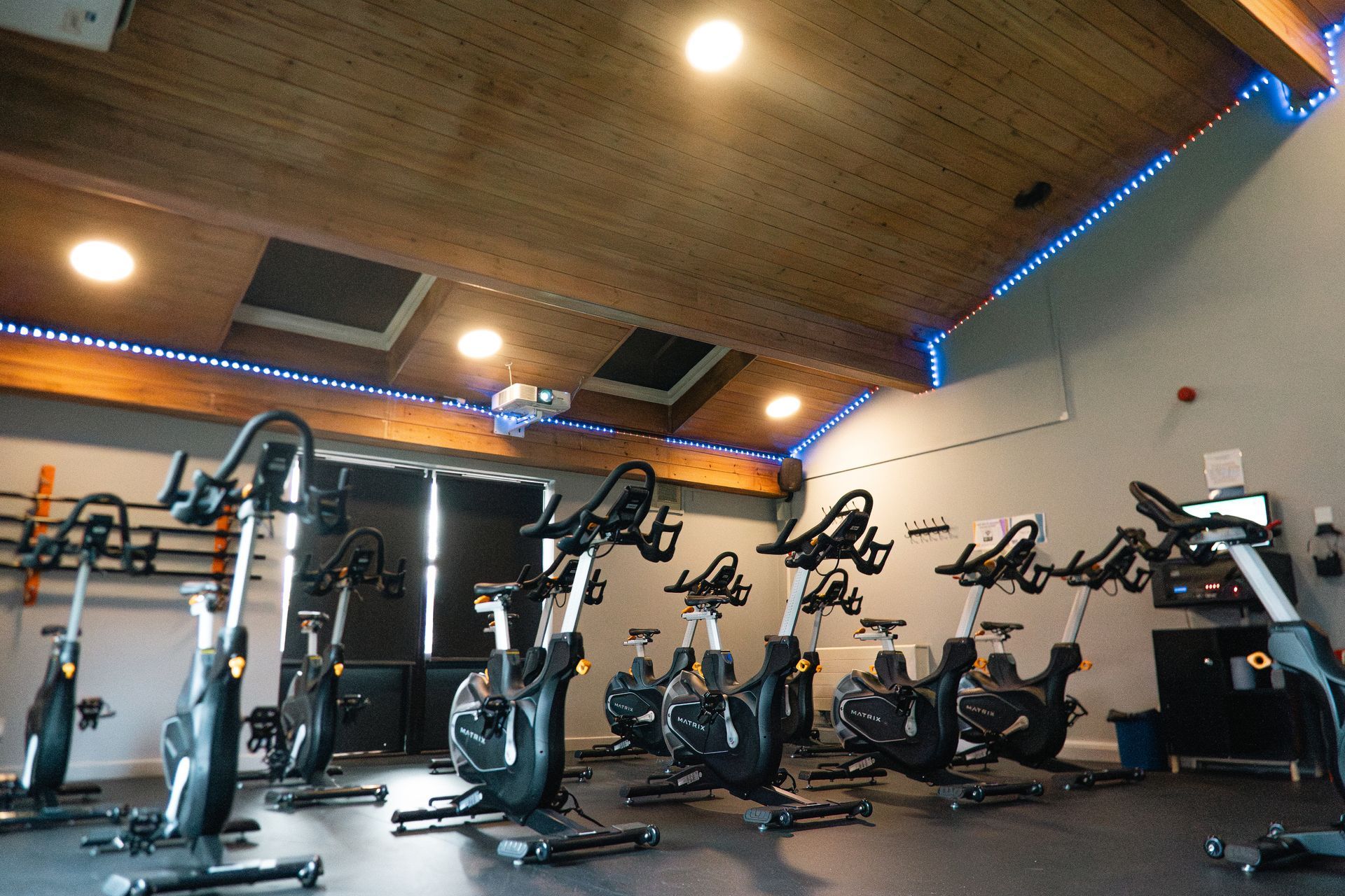 Indoor gym with several stationary bikes under a wood ceiling and blue accent lighting