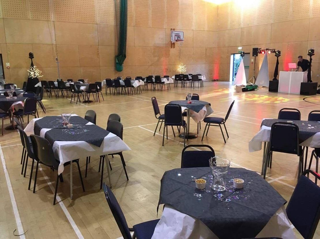 Banquet hall with round tables and black chairs, set for an event under warm lights