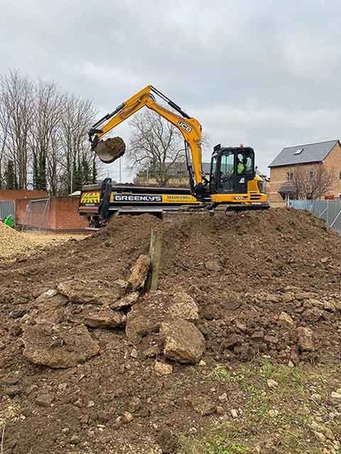A yellow JCB excavator moving a pile of dirt onto a truck
