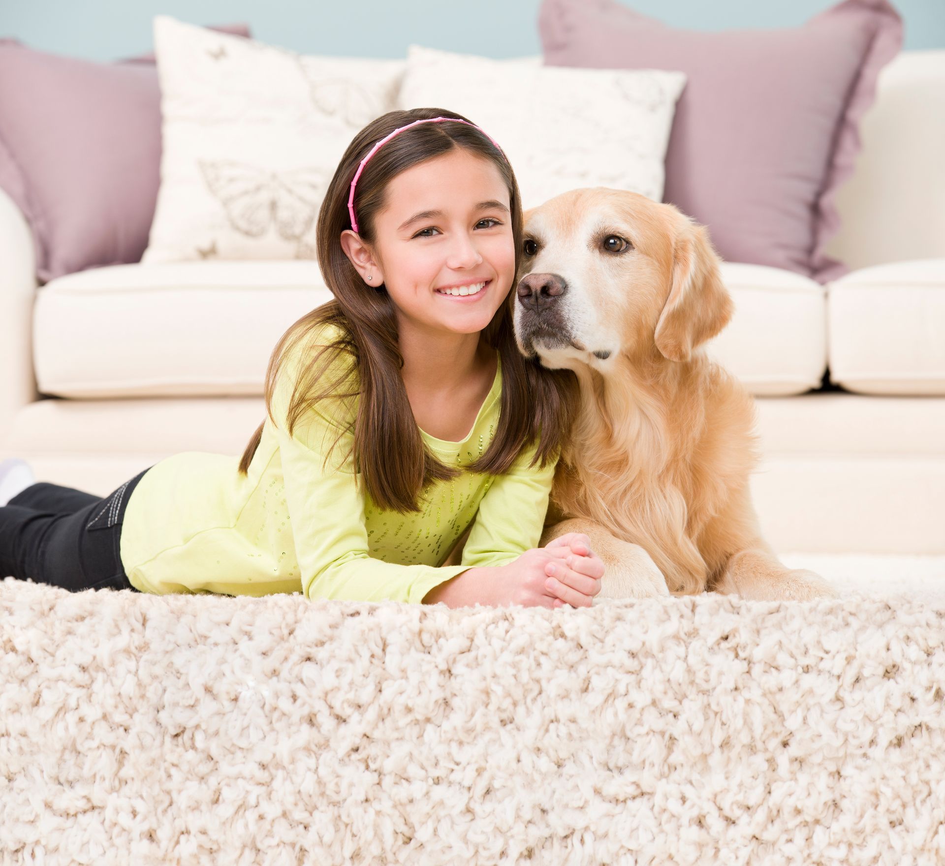 Girl smiles with Golden Retriever on a shaggy rug in front of a couch.