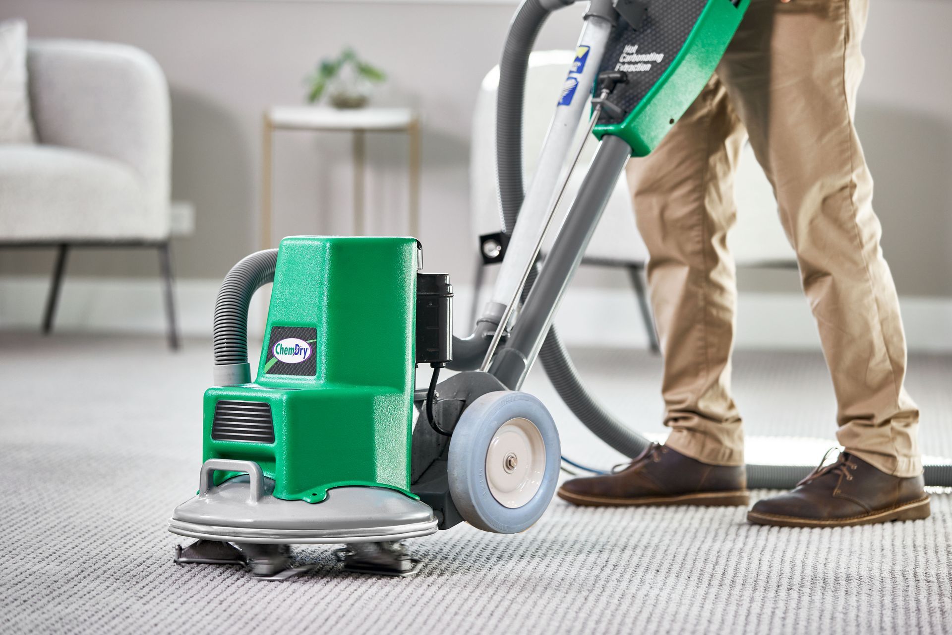 Person operating a green carpet cleaner in a living room.