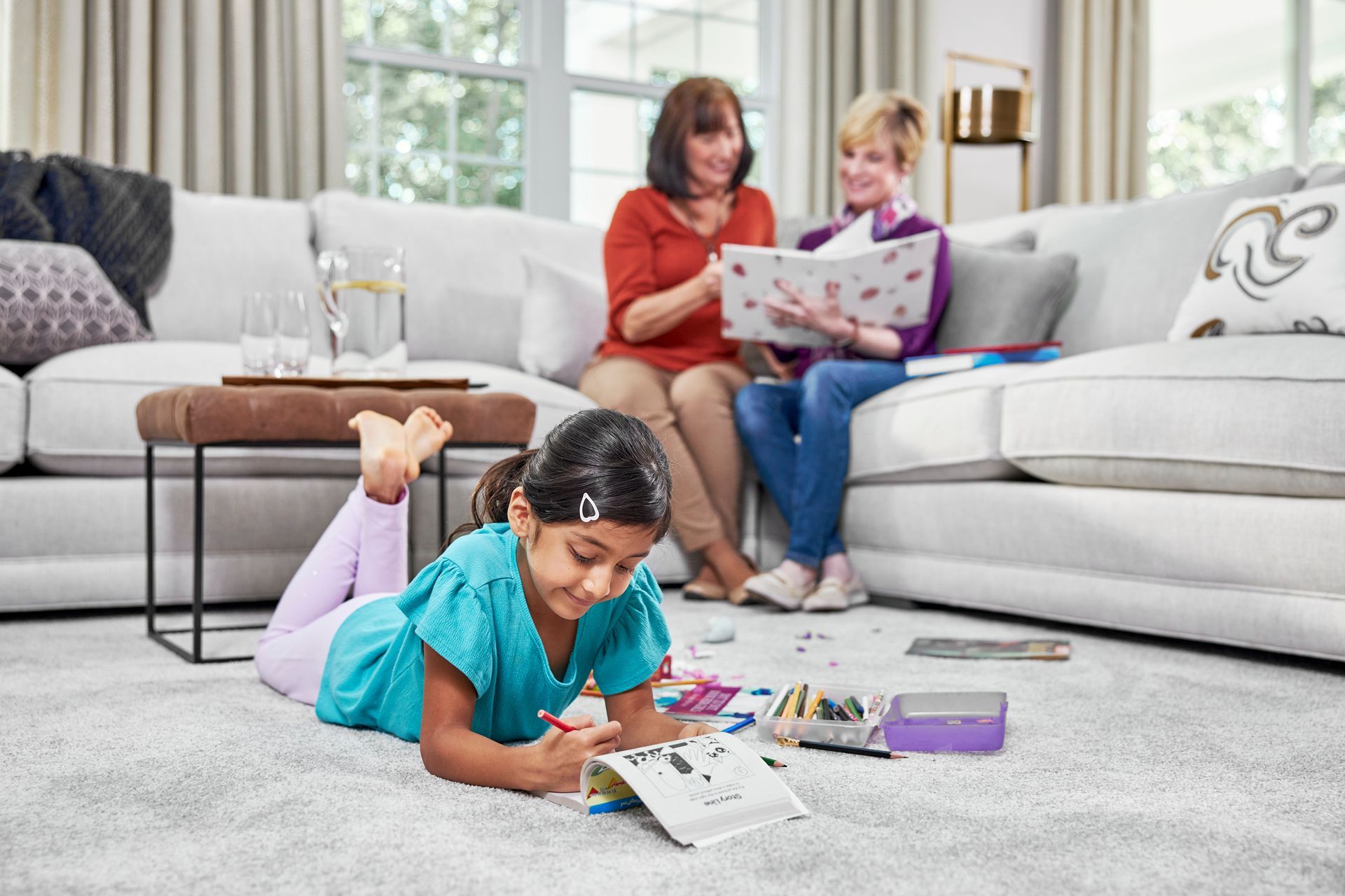 Girl drawing on carpet, two women look at album on sofa. Living room.