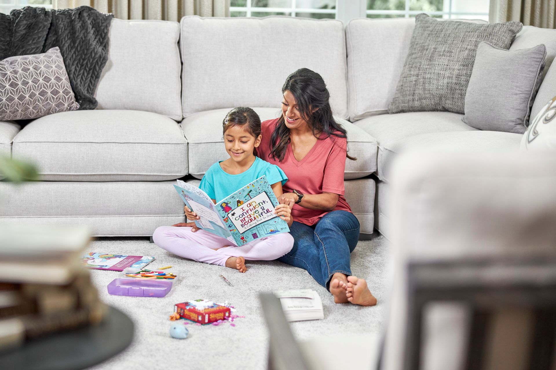 Woman and child sitting on floor, reading a book together in front of a white sectional sofa.