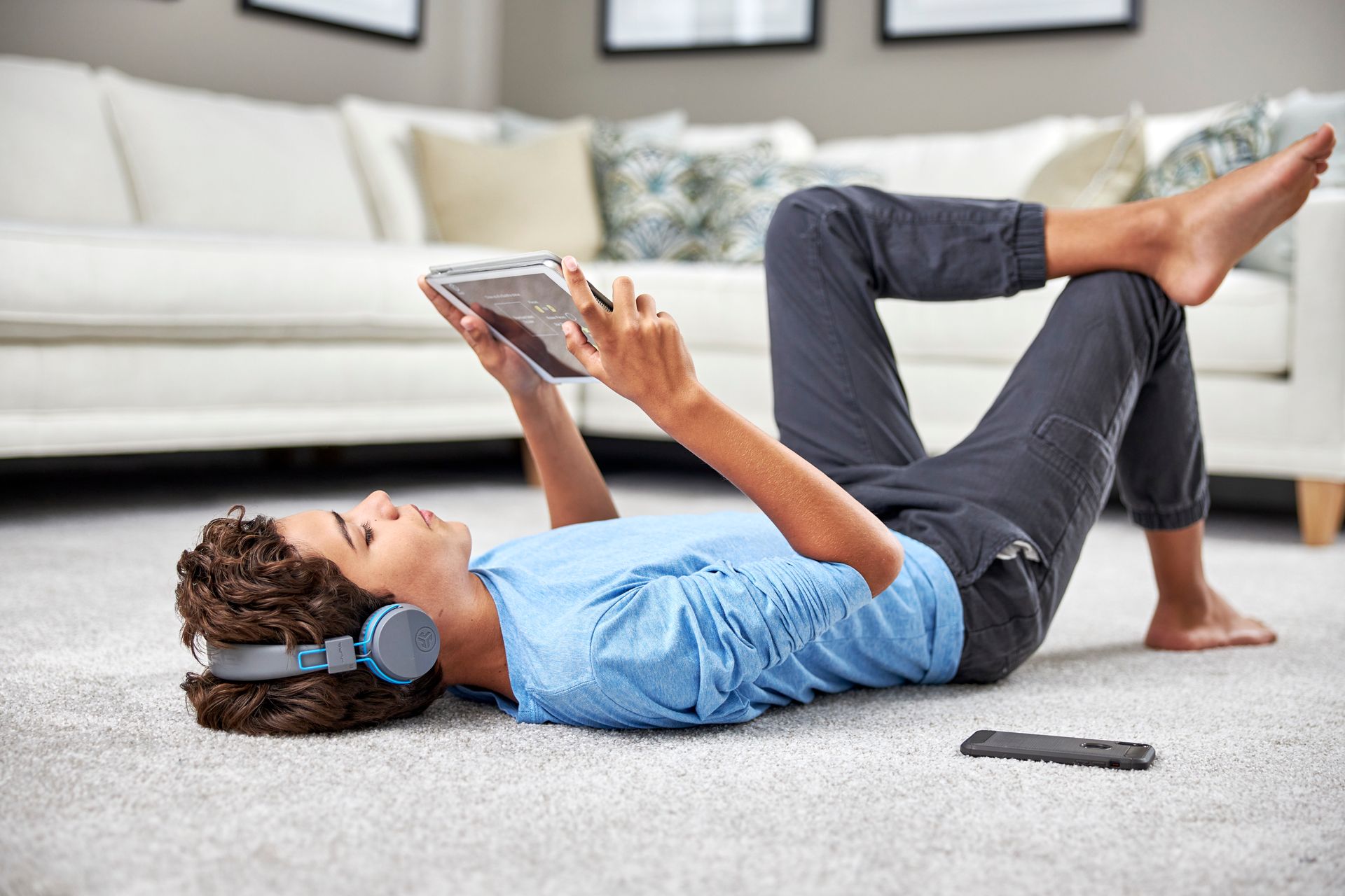 Person lying on floor with tablet, headphones on, feet up.