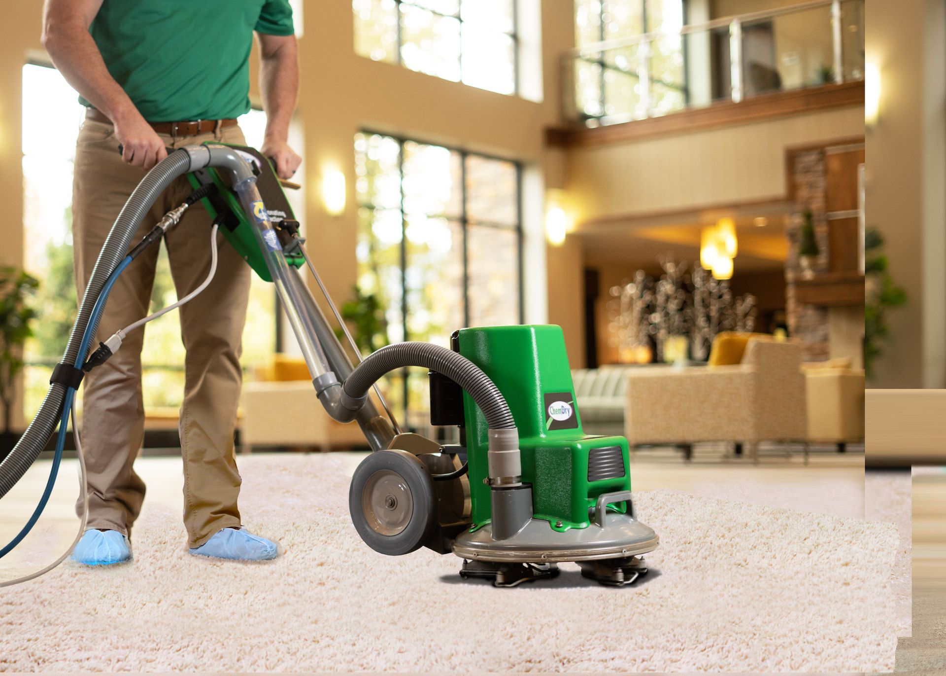 Person cleaning carpet with green industrial machine in a large, bright room.