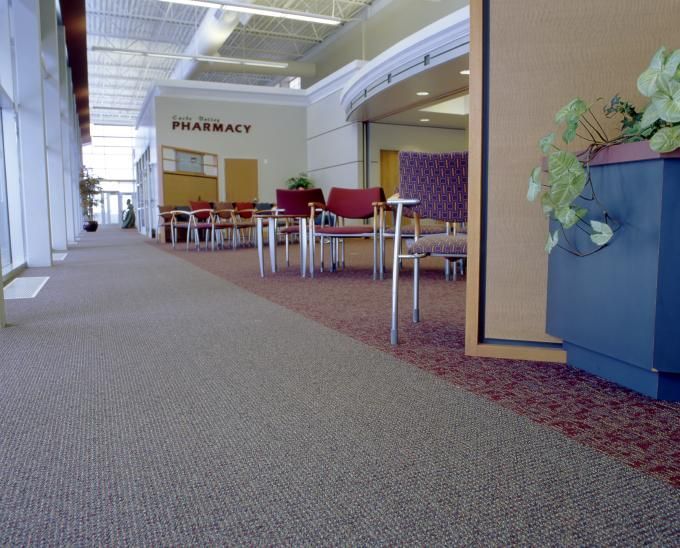 Hallway with tan carpet, chairs and tables. Pharmacy sign visible.